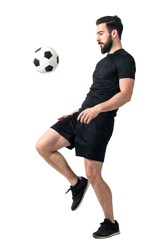 Side view of football or futsal player juggling ball with his knee. Full body length portrait isolated over white background.