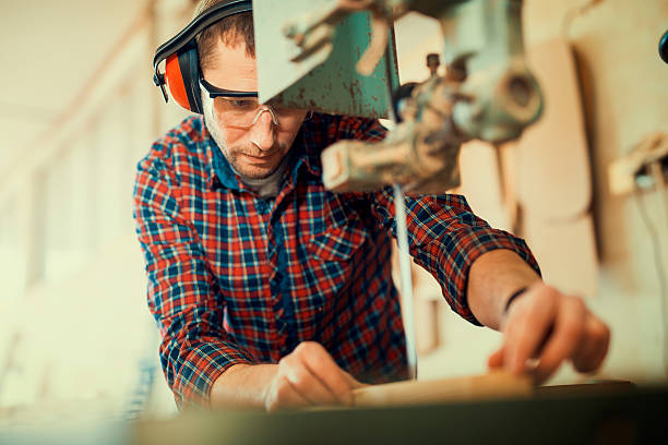 Close up of a young carpenter at work.He is using a bandsaw, also known as a jigsaw or a scroll saw, cuts through a piece of wood.