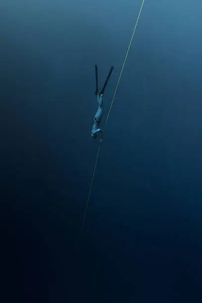Free diver descending along the rope in the depth