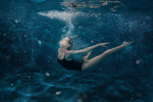 Woman dancing under the water around the air bubbles.