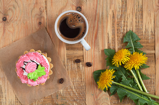 Cup of hot coffee, sweet cake and flowers on old wooden background, top view