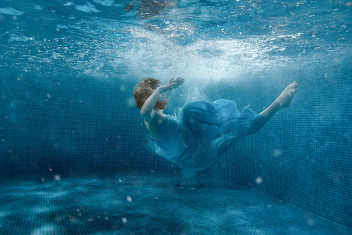 The girl from the fairy tale in a blue dress sinks under water.