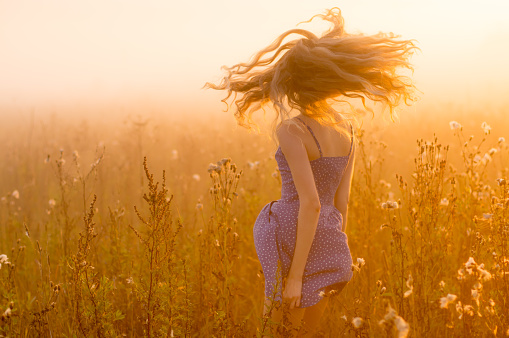 Dancing beautiful girl in fog, field, sun backlight, sunrise, orange colors