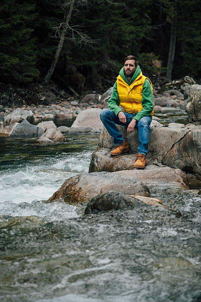 мужчина сидит на скале вблизи реки в горы - river men crossing spirituality стоковые фото и изображения