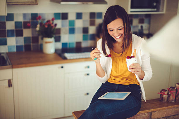 Hispanic woman reading tablet and having breakfast in the kitchen