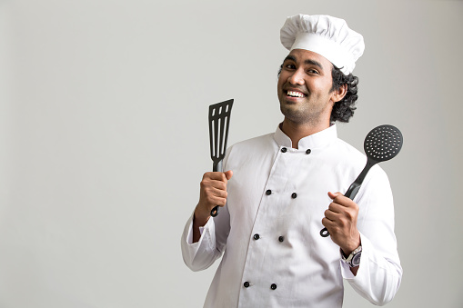 Cheerful happy chef holding kitchen utensil isolated on grey background