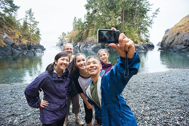 Multi-Ethnic Hiking Family Posing for Selfie on Remote Wilderness Beach A real extended family of multi-ethnic and multi-generational backpackers in the wilderness pose of a selfie on a deserted beach surrounded by islands and forest with the ocean in the background.  Rainy day in a wilderness park.  Whiffen Spit, Sooke, British Columbia, Canada. explorer photos stock pictures, royalty-free photos & images