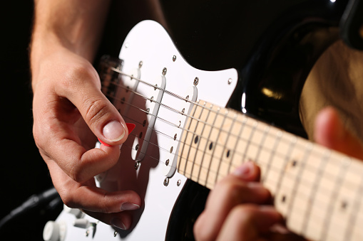 Male hands playing electric guitar with plectrum closeup photo. Learning musical instrument, music shop or school, blues bar or rock cafe, having fun enjoying hobby concept
