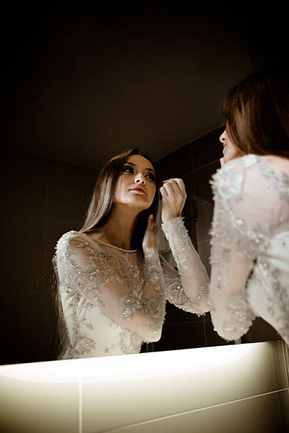 Gorgeous woman with long hair doing makeup in the mirror stock photo