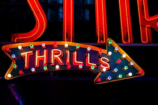 Illuminated neon sign with arrow and text saying 'thrills'. Horizontal image with plenty of copy space.