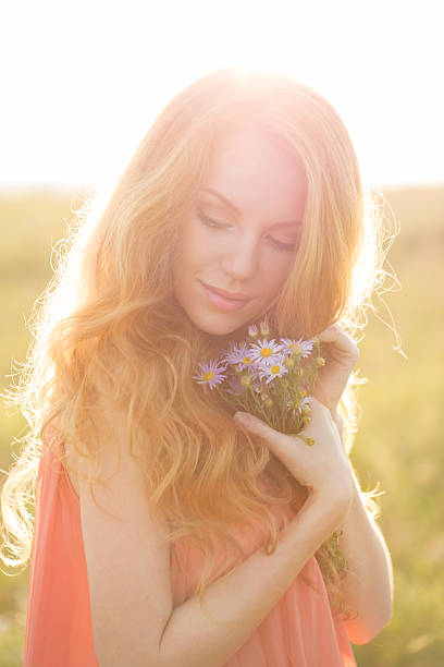 Beautiful girl in the rays of sunset light in the field with a bouquet of wild flowers in their hands.
