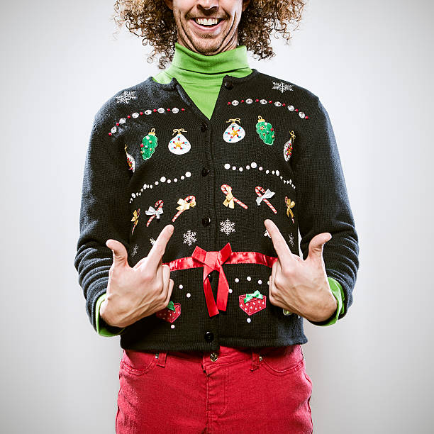 Christmas Sweater Man A man in a knit ugly Christmas cardigan button up sweater, complete with matching red pants and a green turtleneck.  He points proudly to his overly decorated sweater, a smile on his face.  Square crop. christmas sweater stock pictures, royalty-free photos & images