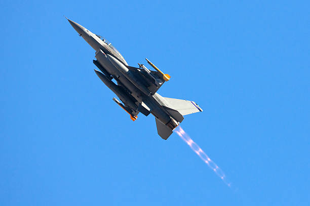 F-16 Fighter aircraft loaded with missiles climbing into the blue sky with glowing afterburner behind it