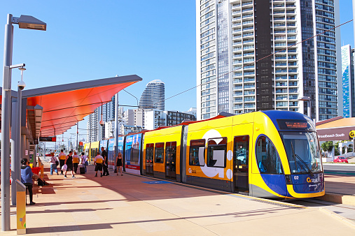 Gold Coast, Australia - November 15, 2014: G:Link light rail service to University Hospital waits at the Broadbeach South terminus on a sunny Saturday afternoon.  Staff in bright yellow shirts are on hand to assist passengers with any questions they have about the new service.  Opened on 20 July 2014, the service uses articulated Bombardier Flexity low-floor accessible trams.