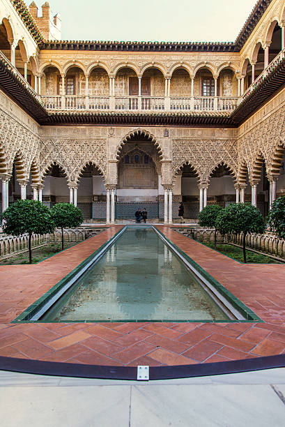 Seville, Spain, Alcazar Seville, Spain. November 15, 2014. Three tourists visit the beautiful "Courtyard of the Maidens" (Patio de las Doncellas) within the royal palace of the Alcazar. The name refers to the legend that the Moors demanded by the Spanish Christian kingdoms, one hundred virgins every year as tribute. alcazar seville stock pictures, royalty-free photos & images
