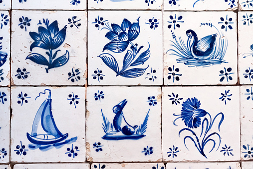 Antique hand made, painted blue & white Delft tile background, with naive symbolic paintings of flowers, a rabbit, a bird and a boat.