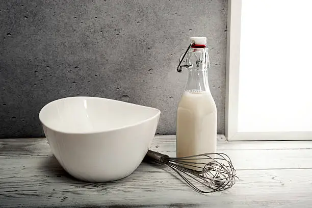 Fresh milk,cream bottle, bowl and wire whisk on window sill