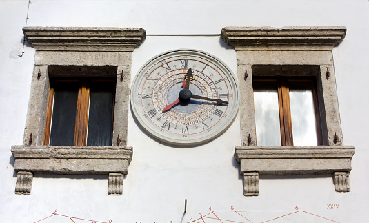 Old stone calendar clock on the external wall of a historic building in Pesariis, Italy