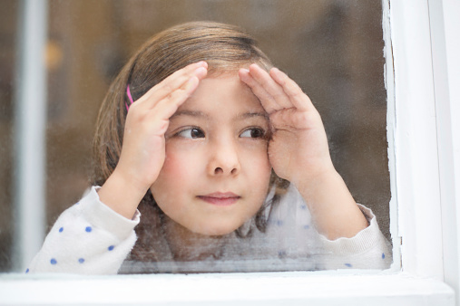 Closeup image of cute little girl looking outside window