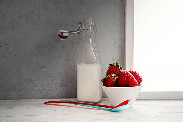Fresh milk,cream bottle on window sill with strawberries in bowl