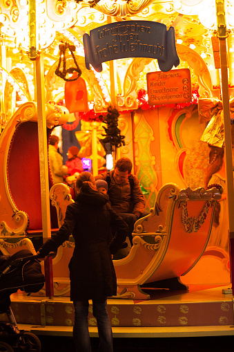 Essen, Germany - December 6, 2014: Night shot of carousel on christmas market in Essen. A man with child is sitting in a carriage. A woman with baby buggy is standing in front of them.