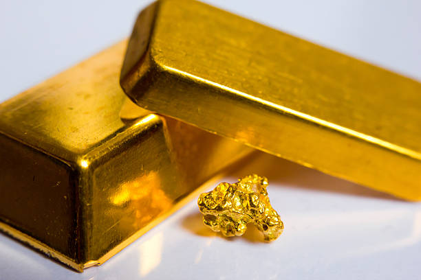 Studio and macro shot of a gold nugget and two ingots isolated on a white background