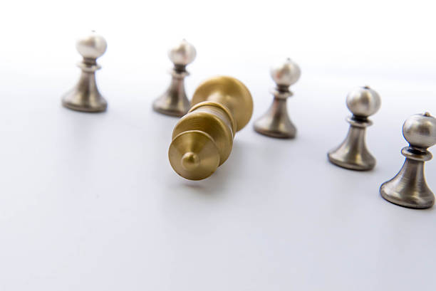 istock chess game - pawns circled around a fallen king 527016811