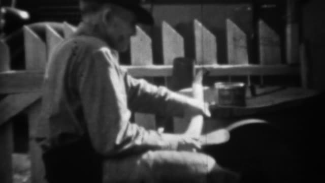 1936: Man sharpening axe on foot powered stone wheel grindstone.