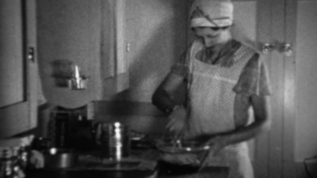 1936: Aproned women cooking in kitchen sifting flour for biscuits.