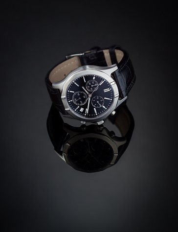 Dark luxury wristwatch on a black reflective surface
