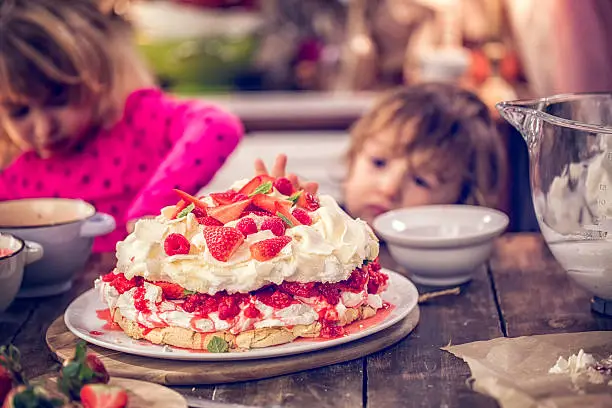 Cute little kids eating delicious Berry Pavlova Cake with fresh strawberries, raspberries, mint leaves and whipped cream.