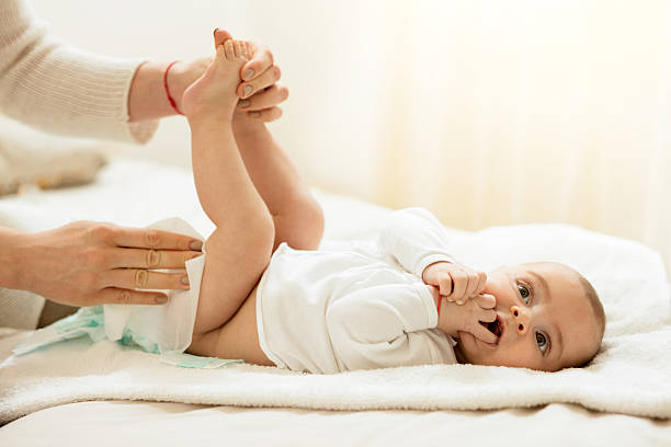 Cute baby in bedroom getting diaper changed. Baby boy lying on the bed with hands in the mouth while getting his diaper changed. ass boy stock pictures, royalty-free photos & images