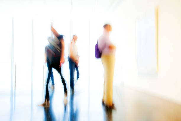 An abstract image of a blurred, unrecognizable people standing, walking in modern, bright interior. In the background are visible large windows.