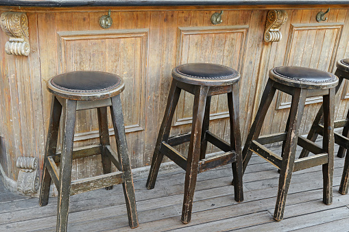 Vintage and rustic wooden bar stools on wooden floor in front of wooden bar with handbag hook hanger
