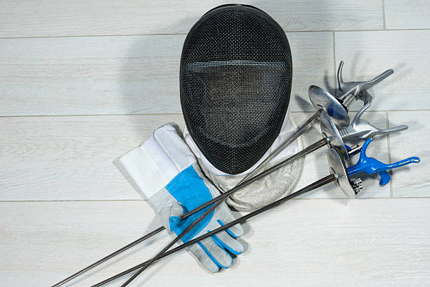 Fencing Foil Equipment Fencing foil equipment. Three fencing foils with pistol grip (sporting weapon), a fencing mask and a blue and white glove on floor. pentathlon stock pictures, royalty-free photos & images