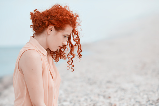 side view of red hair womanon the beach feeling nostalgic and thinking far away.looking down.