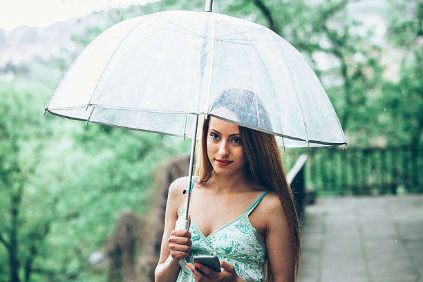 jeune femme avec parapluie sous la pluie en utilisant un téléphone - rain women umbrella parasol photos et images de collection