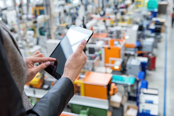 Female manager working on tablet in factory Horizontal color image of businesswoman - unrecognizable person - working with digital tablet in large futuristic factory. Woman standing on top of a balcony, holding touchpad and checking inventory of a manufacturing company on touchscreen tablet. Focus on businesswoman's hands holding black tablet, futuristic machines in background. ordering stock pictures, royalty-free photos & images