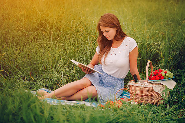 istock Young woman read a book outdoors. Basket with berries behind 527045784