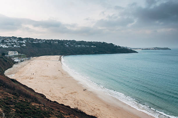 Gloomy day at Carbis Bay near St Ives in Cornwall Gloomy winters day at Carbis Bay beach near to the the popular tourist destination of St Ives, Cornwall, England. It is a cold day in winter with a few groups of people walking on the beach. There are grey clouds in the sky and small waves rolling into shore. st ives cornwall stock pictures, royalty-free photos & images