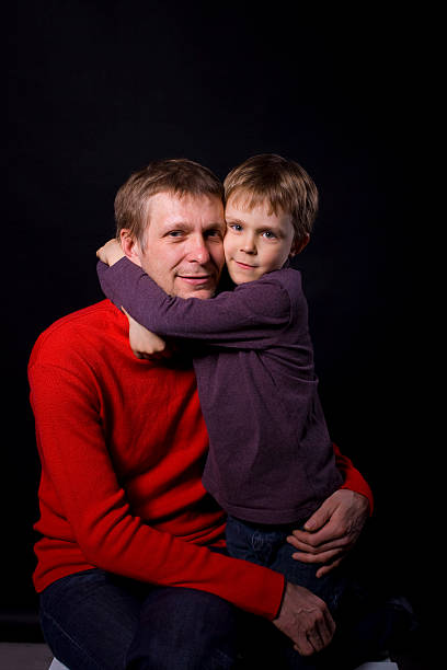 six-year boy hugging his father against a black background in the studio