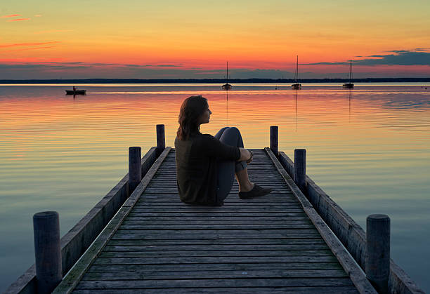 istock Young woman sitting on lakeside jetty at dusk 527051845
