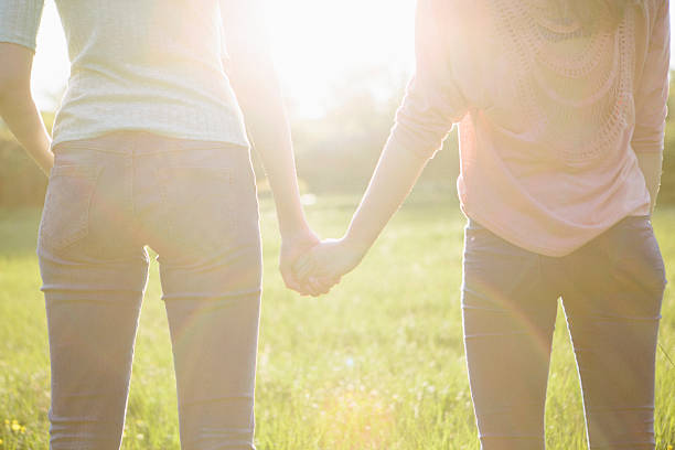 rear view of two young women holding hands, backlit