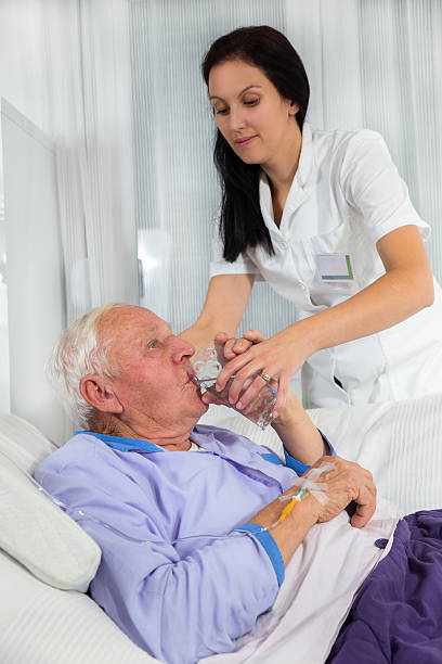 медсестра помогает мужчина в постели, пить воду - infused oil iv drip nurse hospital стоковые фото и изображения