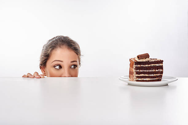 I just can't look away... Shot of a young woman sneak up to a piece of cke standing on a table temptation photos stock pictures, royalty-free photos & images