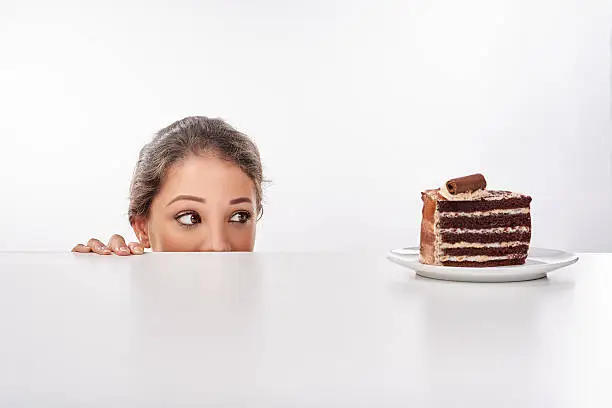 Shot of a young woman sneak up to a piece of cke standing on a table