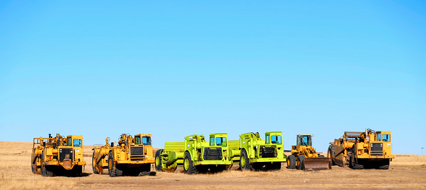 Peyton, Colorado, USA - December 7, 2014: A group of heavy earth moving machinery used in the construction industry parked in an open field, under a clear blue sky.
