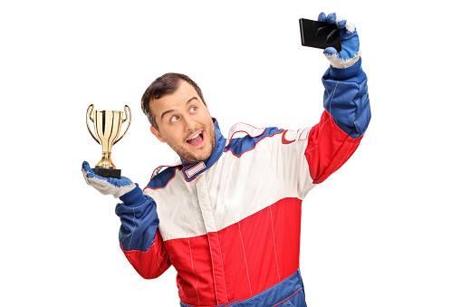 Joyful car racing champion holding a trophy and taking a selfie isolated on white background