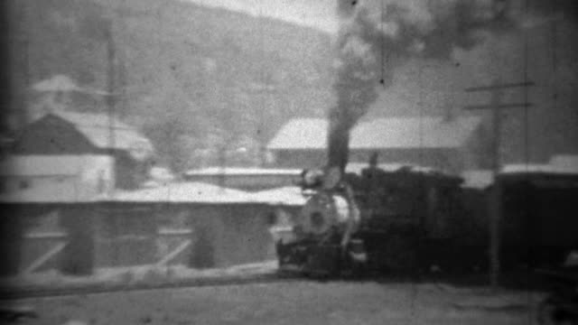 1934: Dirty smoky locomotive train passing small mountain town.