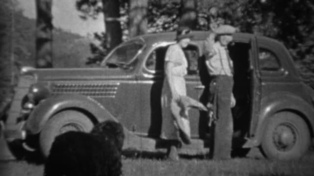 1935: Couple loading black dog into car in mountainous forest.